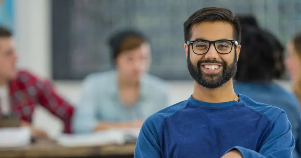 Homem com um óculos sorri em uma sala de estudos