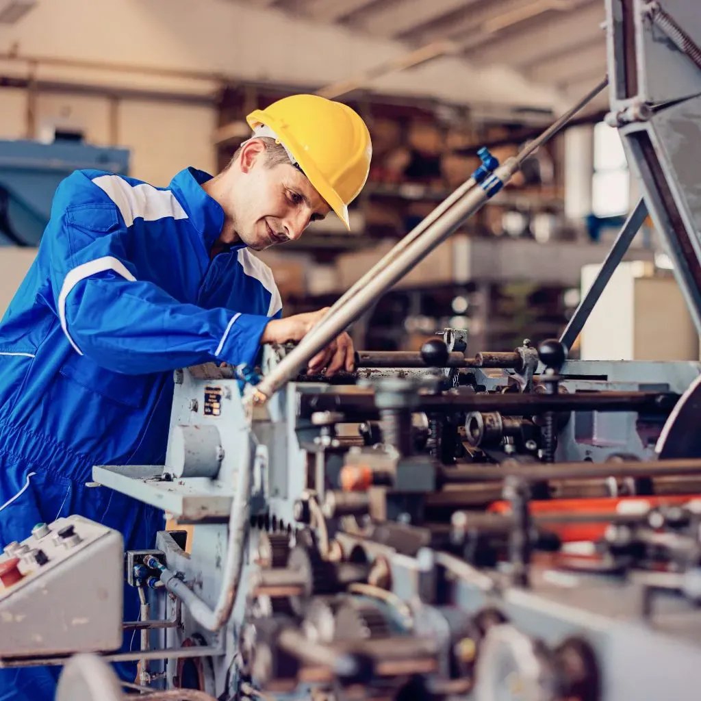 Profissional de capacete e macacão azul fazendo manutenção em uma máquina industrial de eixos e engrenagens