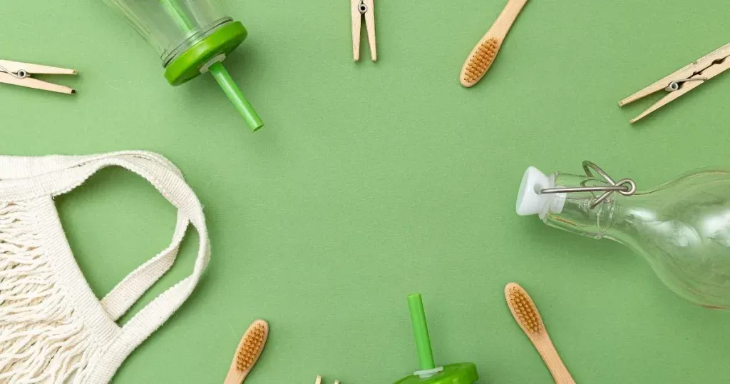 Prendedores de roupa, escova de dente de bambu, garrafinha de água e sacola de pano ecológica sobre uma superfície verde, todos produtos feitos com base dos polímeros biodegradáveis