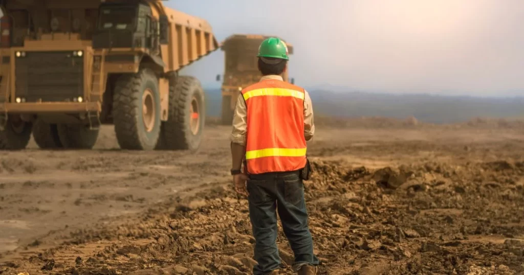 Engenheiro está de pé em um campo aberto com um caminhão de terra a sua frente