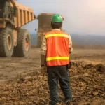 Engenheiro está de pé em um campo aberto com um caminhão de terra a sua frente