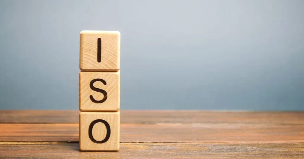 Três dados de madeira empilhados um sob o outro em cima de uma mesa. Cada dado carrega uma letra, que juntas formam a palavra 'ISO' de cima para baixo.